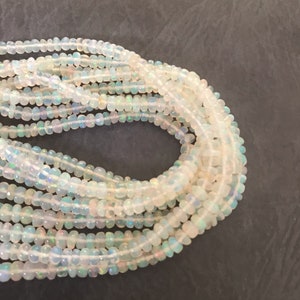 May include: A strand of white opal beads, with a slight iridescent sheen. The beads are small and round, and they are strung together on a clear thread.