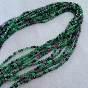 May include: A strand of green and pink gemstone beads. The beads are round and faceted, and they are strung on a clear thread. The beads are approximately 4mm in diameter.