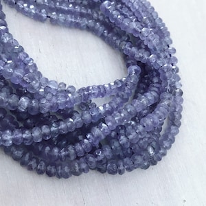 May include: Close-up of multiple strands of faceted, light purple beads. The beads are small and uniform in size, creating a textured surface. The strands are arranged in a layered pattern, showcasing the color and shape of the beads. The overall effect is a display of jewelry components.