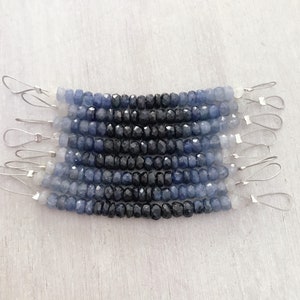 May include: Ten strands of faceted gemstone beads, ranging in color from light blue to dark blue and black. The beads are strung on silver wire with small loops at each end.