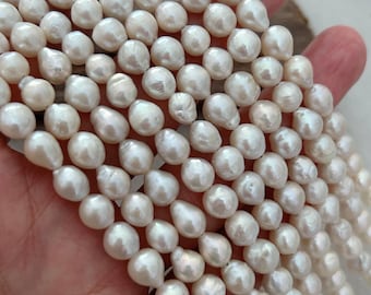 May include: A collection of lustrous, off-white freshwater pearls. The pearls are irregularly shaped, with a smooth, pearlescent surface. Strands of pearls are visible, suggesting they are ready for jewelry making.