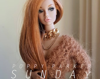 May include: A red-haired doll with a brown fuzzy sweater and gold chain necklaces. The doll has blue eyes and is wearing gold chain necklaces. The text "POPPY PARKER SUNDAY" is visible in the image.