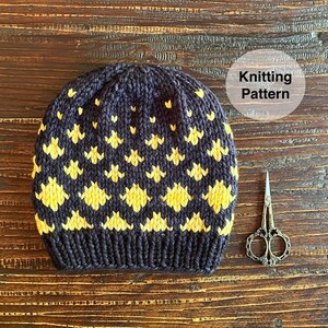 May include: A navy blue knitted hat with a yellow geometric pattern. The hat has a ribbed brim. The image also includes a pair of small scissors and the text "Knitting Pattern".