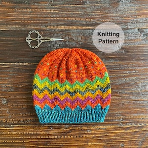 May include: A colorful knitted hat with a zig-zag pattern in shades of orange, yellow, green, blue, and purple. The hat has a textured knit and a pom-pom on top.