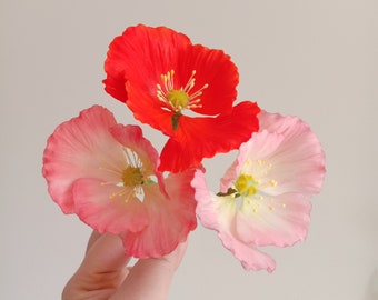 Könnte beinhalten: Drei Seidenmohnblumen, eine rote und zwei rosa, mit zarten Blütenblättern und gelben Zentren.