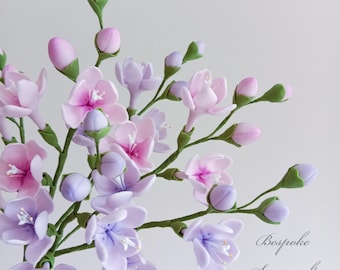 Könnte beinhalten: Ein Strauß zarte Zuckerblumen in Rosa- und Lilatönen. Die Blumen sind in einer Traube angeordnet, einige Knospen sind noch geschlossen. Die Blumen sind aus Fondant und eignen sich perfekt zum Dekorieren von Torten und Cupcakes.