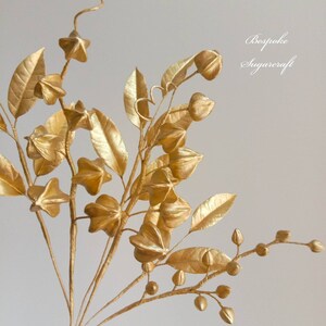 A bouquet of gold-painted sugar berries and leaves. The berries are star-shaped and the leaves are long and narrow. The bouquet is arranged in a vase and is ready to be used as a cake topper or centrepiece.
