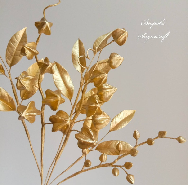A bouquet of gold-painted sugar berries and leaves. The berries are star-shaped and the leaves are long and narrow. The bouquet is arranged in a vase and is ready to be used as a cake topper or centrepiece.