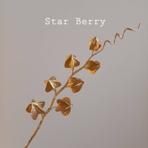 A gold-coloured metallic sugarcraft star berry vine with a curled stem and multiple star-shaped leaves.