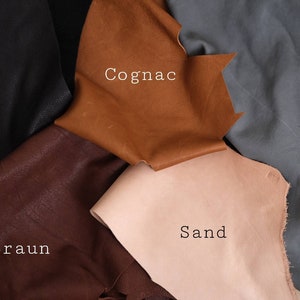May include: Five leather swatches in different colors: black, brown, cognac, sand, and gray. The swatches are labeled with the German words for each color.