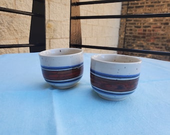 Puede incluir: Dos tazas de té de cerámica blanca con rayas azules y marrones. Las tazas tienen un esmalte moteado.