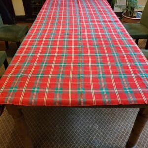 Puede incluir: Un mantel de mesa de cuadros rojos, verdes y dorados sobre una mesa de madera con sillas verdes.