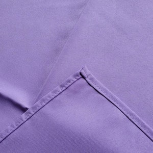 May include: A close-up of a lavender fabric with a visible seam. The fabric has a smooth texture and a slight sheen. The seam is stitched with a matching thread, creating a clean, finished edge.