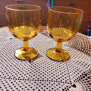 Op de afbeelding: Twee amber glazen kelken met een getextureerd oppervlak staan op een wit gehaakt tafellaken.