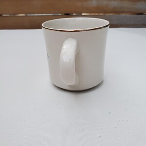 Puede incluir: Una taza de cer&aacute;mica blanca con borde dorado y asa curvada. La taza tiene un dise&ntilde;o sencillo y elegante, apto para caf&eacute; o t&eacute;. La taza est&aacute; sobre un fondo neutro.