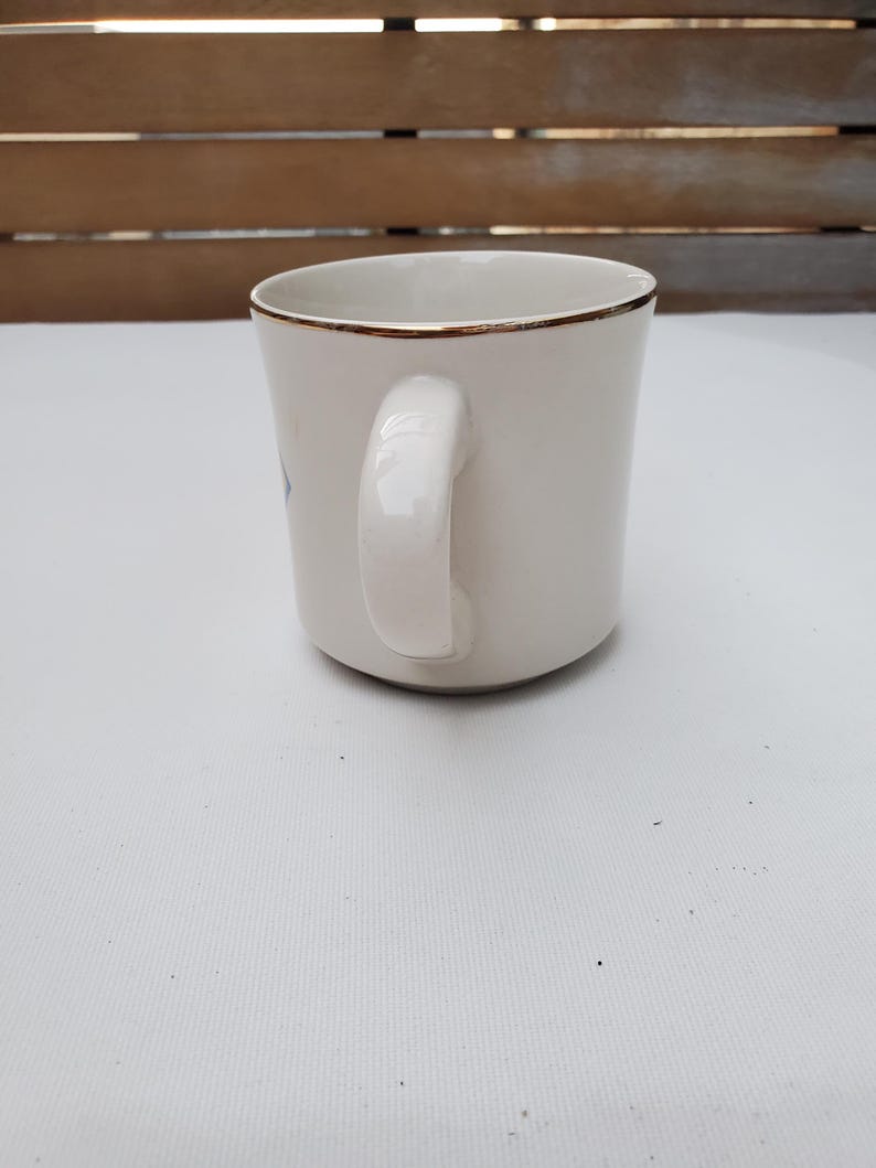 Puede incluir: Una taza de cer&aacute;mica blanca con borde dorado y asa curvada. La taza tiene un dise&ntilde;o sencillo y elegante, apto para caf&eacute; o t&eacute;. La taza est&aacute; sobre un fondo neutro.