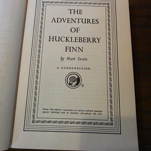 Può includere: La pagina del titolo di un libro intitolato The Adventures of Huckleberry Finn di Mark Twain, A Condensation. Presenta un bordo nero decorativo, un logo circolare con un'illustrazione di profilo e una nota sui riassunti in corsivo.