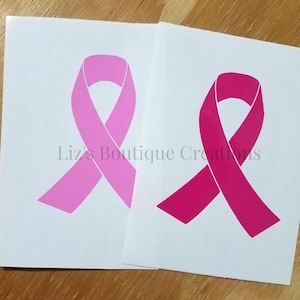 May include: Two pink awareness ribbons on white paper. The ribbon on the left is light pink and the ribbon on the right is a darker shade of pink.