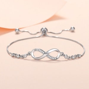 May include: A silver infinity symbol bracelet with clear cubic zirconia stones. The bracelet has an adjustable sliding clasp.