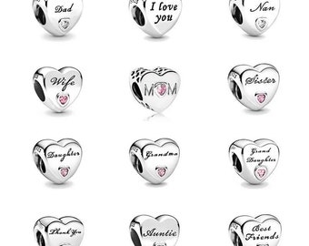 May include: A set of 10 silver heart-shaped charms with various inscriptions, including "Dad", "I love you", "Nan", "Wife", "Mom", "Sister", "Daughter", "Grandma", "Grand Daughter", "Thank You", "Auntie", and "Best Friends". Each charm features a small pink or clear gemstone.