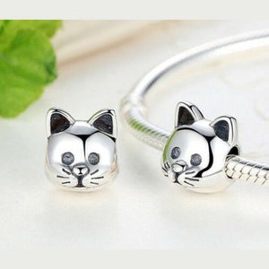 May include: Two silver charm beads in the shape of a cat's face. The beads have black eyes and whiskers.