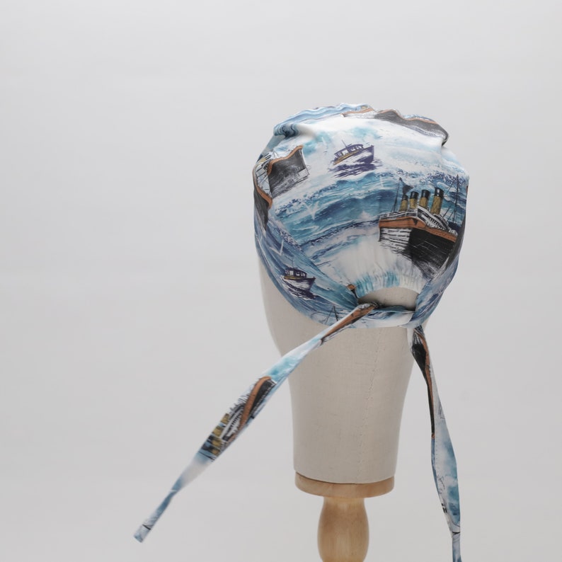 May include: A white and blue patterned bandana with a design of ships and waves. The bandana has two long ties that can be tied at the back of the head.