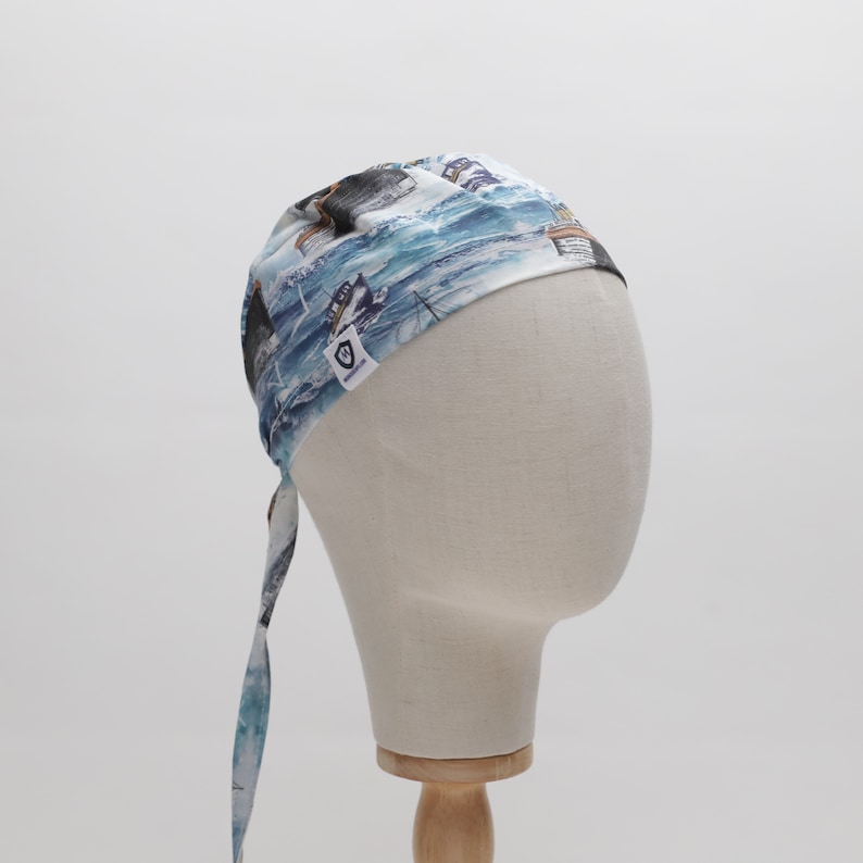 May include: A blue and white patterned bandana with a nautical theme. The bandana has a tie at the back and features a small white label with a logo.