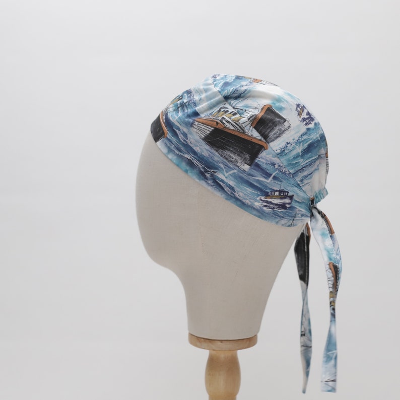 May include: A blue and white bandana with a nautical print of ships and waves. The bandana is tied on a mannequin head.