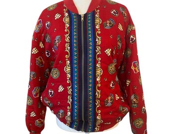 May include: Red bomber jacket with a repeating pattern of crests, shields, and decorative elements. The jacket features a full zipper and a striped design down the center with gold, blue, and brown accents. The jacket has a ribbed collar and cuffs.
