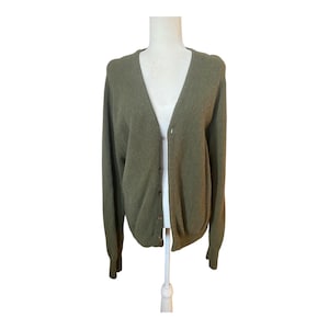Könnte beinhalten: Olivgrüner Cardigan mit V-Ausschnitt und langen Ärmeln. Der Knopf-Pullover wird auf einer weißen Schaufensterpuppe präsentiert. Das Strickware ist einfarbig und scheint aus einem weichen Material zu sein. Der Cardigan ist ca. 70 cm lang.