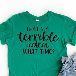 K&ouml;nnte beinhalten: Ein gr&uuml;nes T-Shirt mit dem Text "That's a terrible idea - what time?" in Schwarz gedruckt.