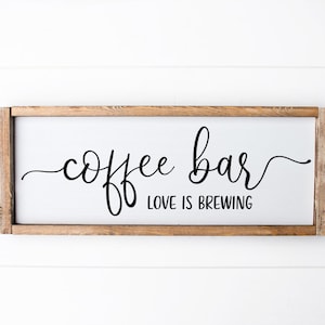 K&ouml;nnte beinhalten: Rechteckiges Holzschild mit wei&szlig;em Hintergrund und braunem Rahmen. Auf dem Schild steht "coffee bar" in Schreibschrift, darunter "LOVE IS BREWING" in kleinerer Schrift. F&uuml;r K&uuml;che oder Essbereich.
