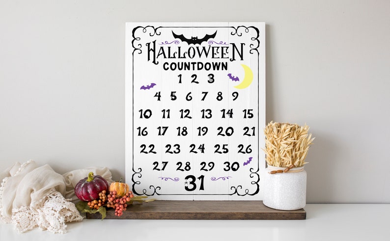 以下が含まれることがあります： 白い木製の看板に、黒い文字で「HALLOWEEN COUNTDOWN」と1から31までの数字が書かれています。看板には紫色のコウモリと黄色の三日月があります。