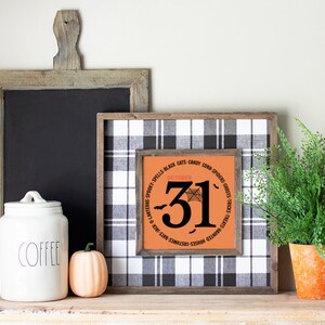 May include: A Halloween-themed display featuring a framed sign with "October 31" and a spiderweb design, set against a black and white plaid background. A wooden chalkboard, a white coffee jar, and a small pumpkin are also present. A potted fern adds a touch of greenery.