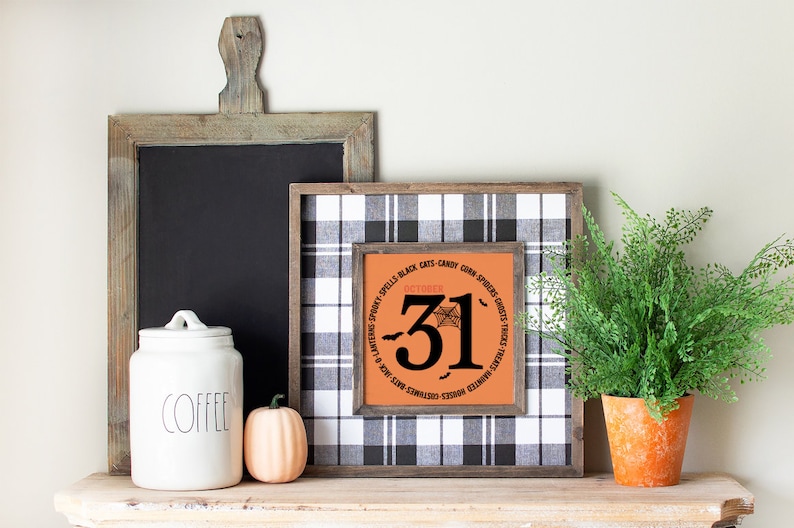 May include: A Halloween-themed display featuring a framed sign with "October 31" and a spiderweb design, set against a black and white plaid background. A wooden chalkboard, a white coffee jar, and a small pumpkin are also present. A potted fern adds a touch of greenery.