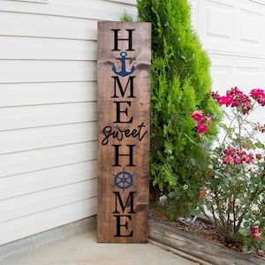 Puede incluir: Un letrero de madera con las palabras "Home Sweet Home" escritas en letras negras. El letrero también presenta un ancla azul y un timón de barco azul.