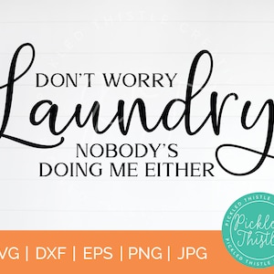 May include: A black and white graphic design with the text "Don't Worry Laundry Nobody's Doing Me Either". The design is on a white wood background. A teal blue circle with the text "Pickled Thistle Creative" is in the lower right corner.