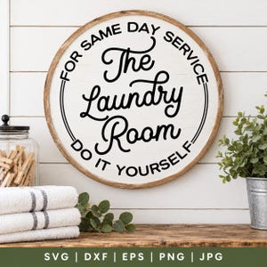 May include: A round white wooden sign with a brown frame featuring black text that reads: FOR SAME DAY SERVICE, The Laundry Room, DO IT YOURSELF. The sign is displayed with a glass jar of wooden clothespins and a small green plant.