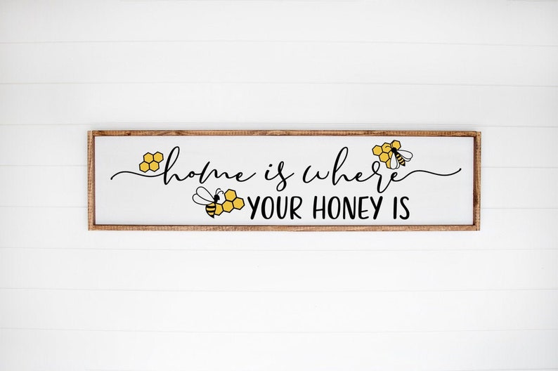 May include: A wooden sign with the text "home is where your honey is" in black script. The sign is decorated with three yellow and black bees and honeycomb.