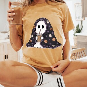 Halloween ghost PNG clipart with a cute ghost wrapped in a patterned blanket and holding a cold coffee cup with a striped straw.
