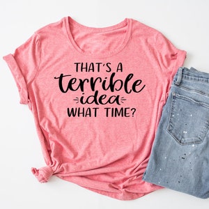 K&ouml;nnte beinhalten: Ein pinkfarbenes T-Shirt mit dem Text "That's a terrible idea - what time?" in Schwarz.