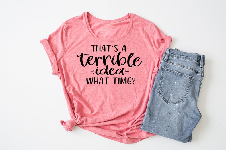 K&ouml;nnte beinhalten: Ein pinkfarbenes T-Shirt mit dem Text "That's a terrible idea - what time?" in Schwarz.