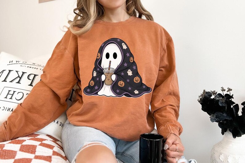 Spooky season digital PNG with a cozy ghost, iced drink, black Halloween blanket, orange pumpkins, cream ghosts, and purple star details.