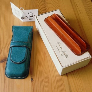 May include: Two leather pen cases, one teal blue and one brown, with the text "Grateful Leather Handcrafted" on the box.