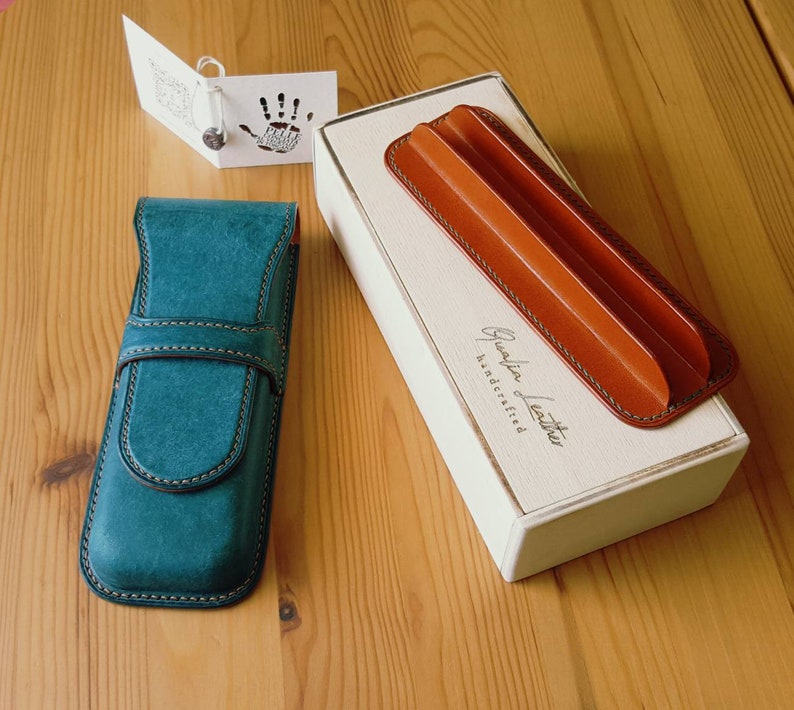 May include: Two leather pen cases, one teal blue and one brown, with the text "Grateful Leather Handcrafted" on the box.