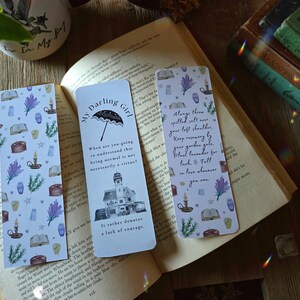May include: Three decorative bookmarks with whimsical designs and text, resting on an open book. One bookmark reads "My Darling Girl" with an umbrella illustration. The other two feature botanical and celestial patterns with quotes.