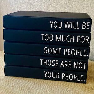 May include: A stack of four black decorative books with white text. The text reads: "YOU WILL BE TOO MUCH FOR SOME PEOPLE. THOSE ARE NOT YOUR PEOPLE."