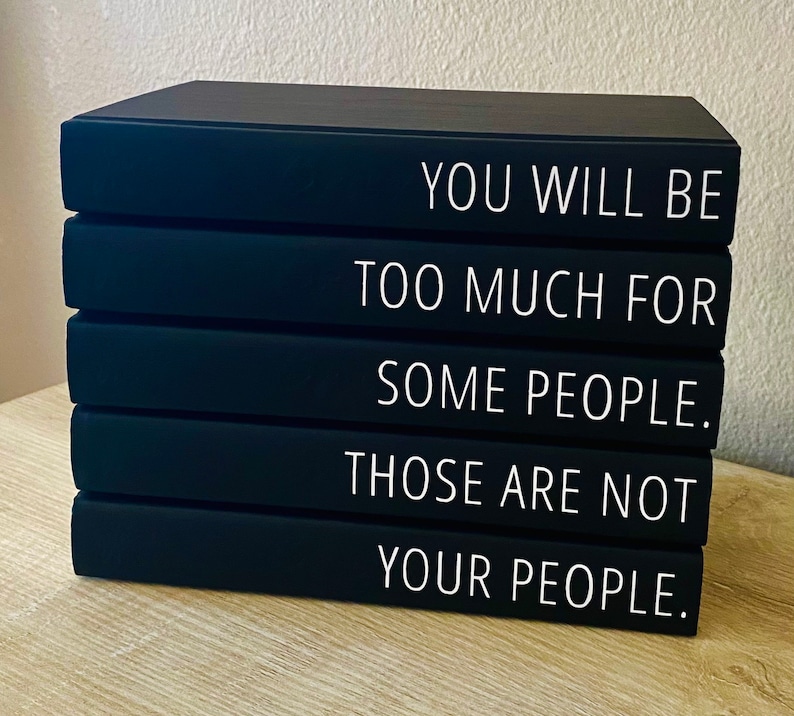 May include: A stack of four black decorative books with white text. The text reads: "YOU WILL BE TOO MUCH FOR SOME PEOPLE. THOSE ARE NOT YOUR PEOPLE."