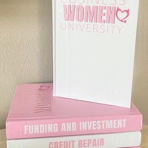 May include: A stack of books with the title "BUSINESS WOMEN UNIVERSITY" in pink lettering. The top book is white, and the others are pink. The titles "FUNDING AND INVESTMENT", "CREDIT REPAIR", and "FINANCIAL LITERACY" are visible.