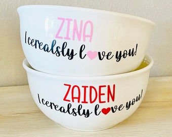 May include: Two white ceramic bowls with black lettering that says "I cerealsly love you!"  The top bowl has the name "ZINA" in pink lettering. The bottom bowl has the name "ZAIDEN" in red lettering.